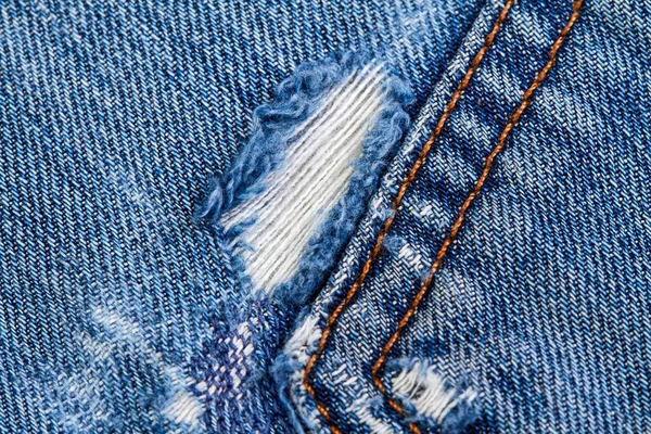 Part of a blue denim jeans background pocket with damage and seams with orange thread stitches