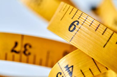 Beyaz zemin üzerinde uzunluk ve genişlik ölçümü için siyah şekilli sarı renkli santimetre. Tasarımınız için terzinin şeridini ölçüyorum. Yakın çekim, seçici odaklanma