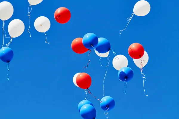 Multicolored helium balloons flying up in the blue sky