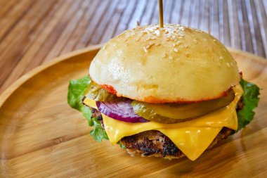 Tahta tabakta sığır eti, peynir ve marul yapraklarıyla hamburger. Yakın çekim, seçici odaklanma