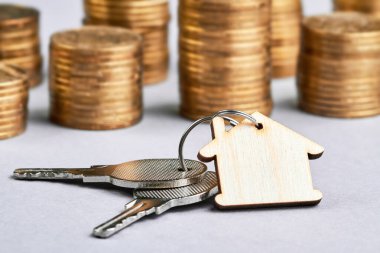 Ahşap bir ev şeklinde süs eşyası. Arka planda para yığınları olan dairenin anahtarları.