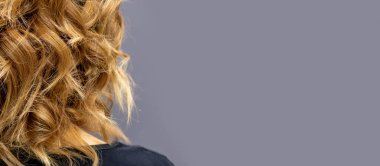 Uzun kahverengi kıvırcık saçlı kadının arka planı koyu bir arka planda duruyor.