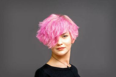 Güzel beyaz kadın portresi. Pembe kısa saç stili. Arka planda koyu renk.