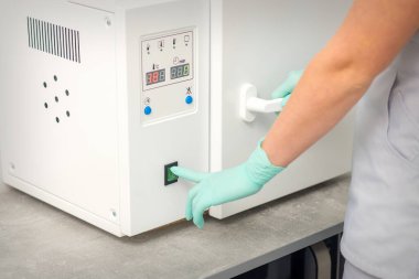 Koruyucu eldivenli güzellik uzmanı, depilasyon prosedüründen önce aletleri dezenfekte etmek için makineyi çalıştırıyor