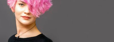 Güzel beyaz kadın portresi. Pembe kısa saç stili. Arka planda koyu renk.