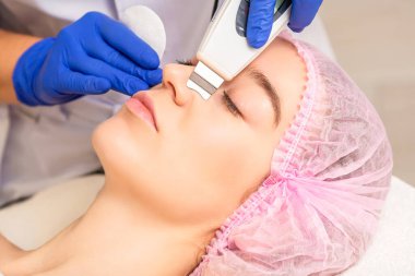 Kozmetik ofisinde ultrason yüz derisi yüzülen ve ultrasonik ekipmanla yüz derisi yüzülen güzel bir genç kadın.