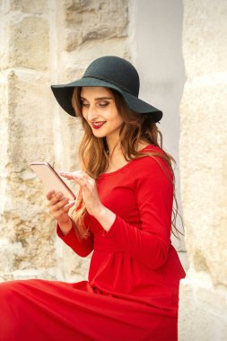 Kırmızı ceketli, siyah şapkalı ve akıllı telefonlu gezgin bir beyaz kadın.