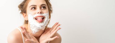 Yüzünde tıraş köpüğü olan güzel, genç, gülümseyen beyaz bir kadının portresi beyaz arka planda dilini dışarı çıkardı.