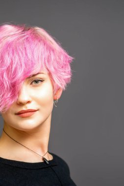 Güzel beyaz kadın portresi. Pembe kısa saç stili. Arka planda koyu renk.