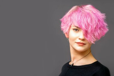 Güzel beyaz kadın portresi. Pembe kısa saç stili. Arka planda koyu renk.