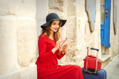 Kırmızı ceketli, siyah şapkalı ve akıllı telefonlu gezgin bir beyaz kadın.
