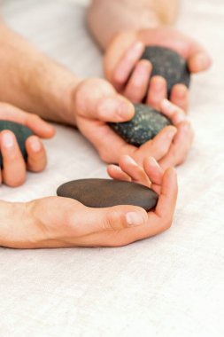 Erkek masörlerin dört eli beyaz havluyla kaplıca taşlarını tutuyor. Taş masajı konsepti