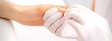 Manikür ustası güzellik salonunda kadın parmaklarının ucundaki nemlendiriciyi siliyor.