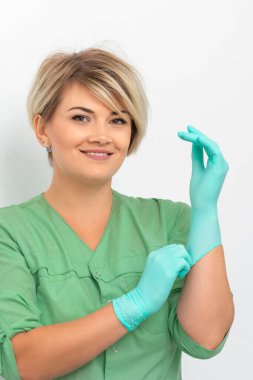 Doktor güzellik uzmanı steril mavi eldivenler giyer gülümseyerek müşterileri beyaza yatırmaya hazırlanır.