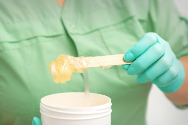 Çubuktaki tüy dökülmesi için sıvı sarı şeker macunu bir güzellik uzmanının ellerinde kavanoza akıyor.