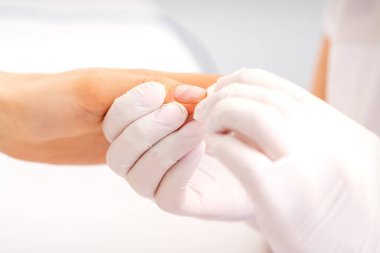 Manikür ustası güzellik salonunda kadın parmaklarının ucundaki nemlendiriciyi siliyor.