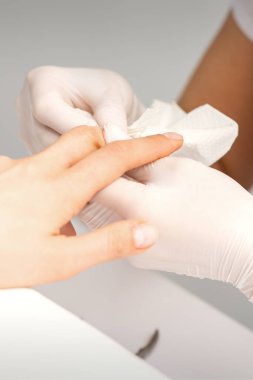 Manikür ustası güzellik salonunda kadın parmaklarının ucundaki nemlendiriciyi siliyor.