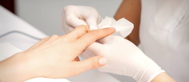 Manikür ustası güzellik salonunda kadın parmaklarının ucundaki nemlendiriciyi siliyor.