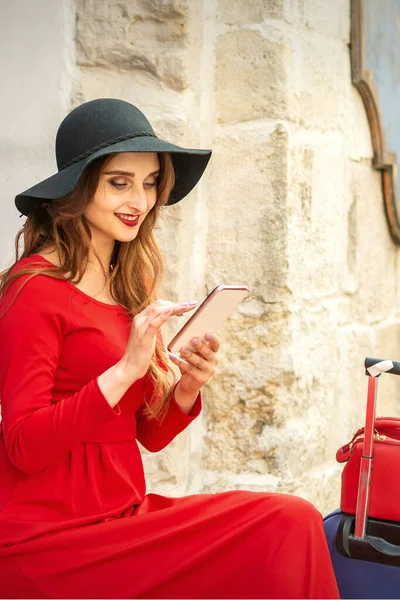 Kırmızı ceketli, siyah şapkalı ve akıllı telefonlu gezgin bir beyaz kadın.
