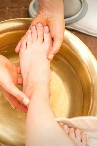 Washing female foot in a special container by male masseur in spa salon