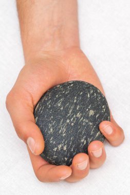 Masörün eli beyaz arka planda masaj taşını tutuyor.