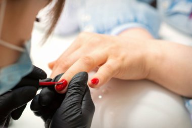 Bir kadının tırnaklarını boyamak. Siyah eldivenli manikürcünün elleri kuaförde kadın tırnaklarına kırmızı oje sürüyor.