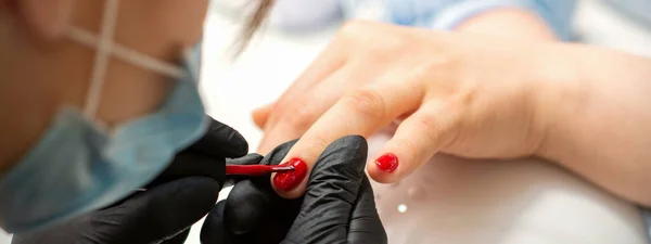 画一个女人的指甲美容院内戴黑色手套的美容师手在女性指甲上涂红色指甲油 — 图库照片