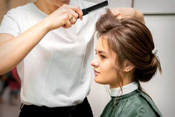長い髪を持つ美しいブルネットの若い女性のためのヘアスタイルを行うプロの美容師 ファッションと美しさの概念 — ストック写真