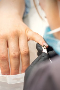 Manikür ustası tırnak derisini bir dişçiyle yüzüyor. Güzellik salonunda manikür temizliği yapıyor.