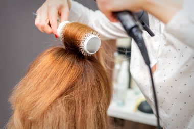 Saç kurutma makinesi ve yuvarlak fırçayla kurutulmuş kızıl saçlar.