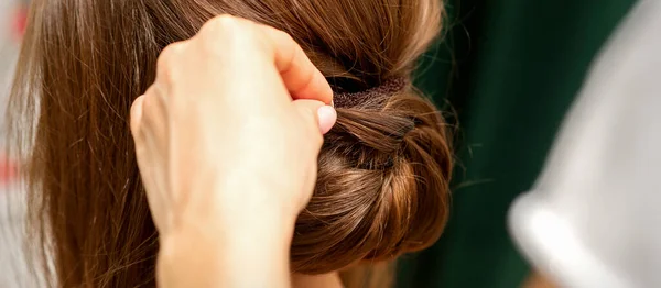 发型师的手在美容院里做着一个无法辨认的年轻黑发女人的法国式扭曲发式 — 图库照片