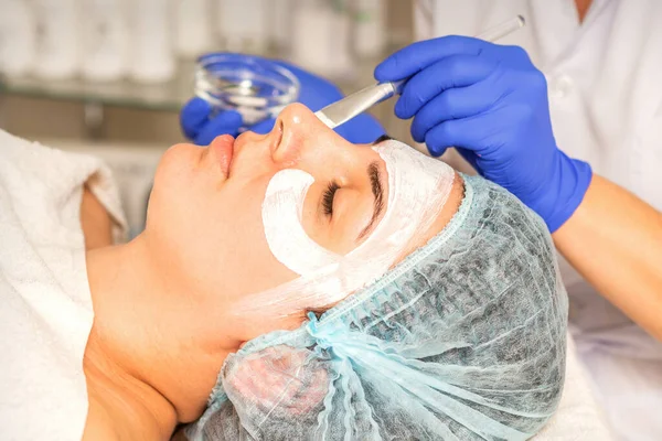 Face peeling at the beautician. Facial treatment. The beautician applies a cleansing face mask to the female patient