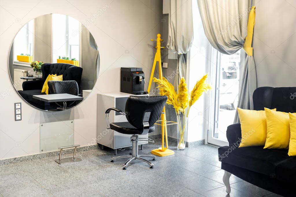 Modern small bright hair and beauty salon in black and yellow colors with gray walls and floor and black sofa with yellow cushions