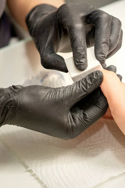 プロのマニキュア師の白人の手の近くに若い女性の爪を提出しています ネイルサロンでネイルファイルを持つ美容師によってマニキュアを受けて若い白人女性 — ストック写真