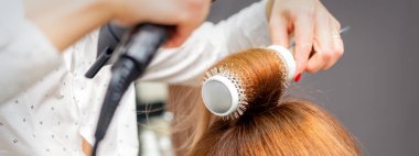 Saç kurutma makinesi ve yuvarlak fırçayla kurutulmuş kızıl saçlar.