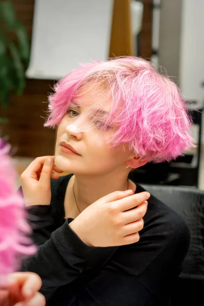 美しいです若いですCaucasian女性とともに新しい短いピンクの髪型見ます彼女の反射でザミラーチェックヘアスタイルでザ美容師サロン — ストック写真