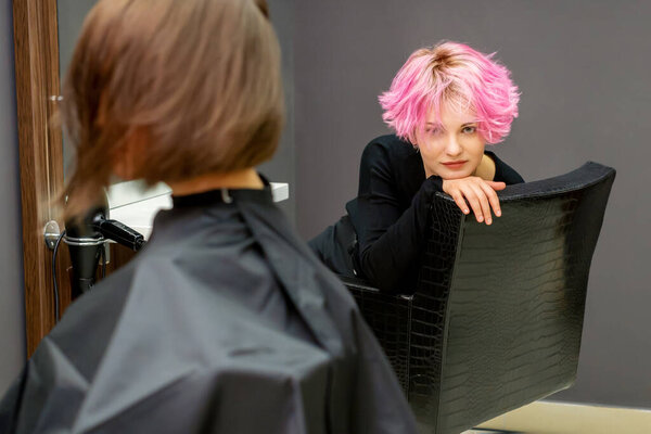 Portrait of a beautiful young caucasian woman with a new short pink hairstyle sitting in a chair at a hairdresser salon