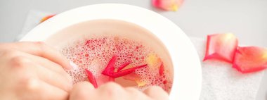 Kaplıcada pembe gül yaprakları olan bir kase suyun içindeki kadın elleri