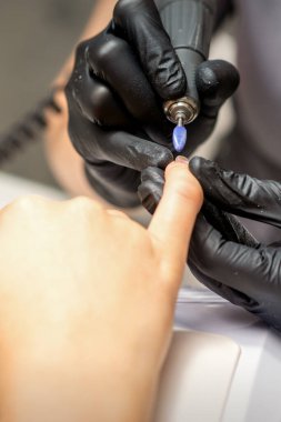 Manikür ustası manikürcüde elektrikli tırnak törpüsü kullanıyor.