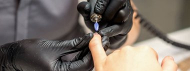 Manikür ustası manikürcüde elektrikli tırnak törpüsü kullanıyor.