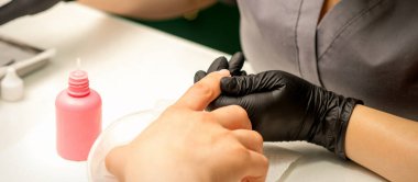 Close up professional manicure master holds the female hand of the customer and disinfects nails in a nail salon