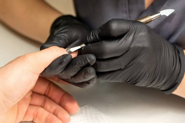 Profesyonel manikürcü ustası manikürcüde manikürcüyü kullanırken müşteri elini tutuyor.