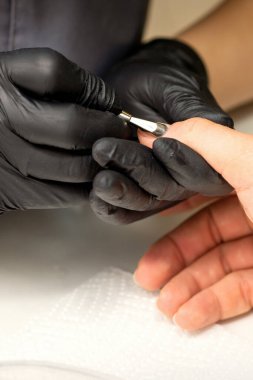 Profesyonel manikürcü ustası manikürcüde manikürcüyü kullanırken müşteri elini tutuyor.