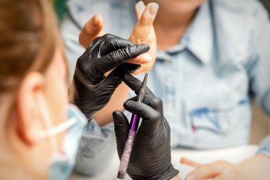 Manikür boyama sanatı. Manikür ustası tırnak ucuna ince bir fırçayla resim çiziyor.