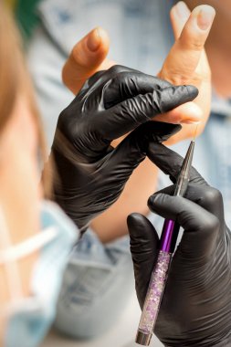 Manikür boyama sanatı. Manikür ustası tırnak ucuna ince bir fırçayla resim çiziyor.