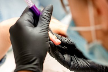 Manikür boyama sanatı. Manikür ustası tırnak ucuna ince bir fırçayla resim çiziyor.