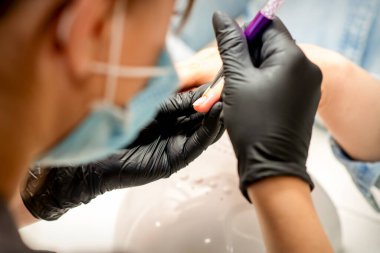 Manikür boyama sanatı. Manikür ustası tırnak ucuna ince bir fırçayla resim çiziyor.