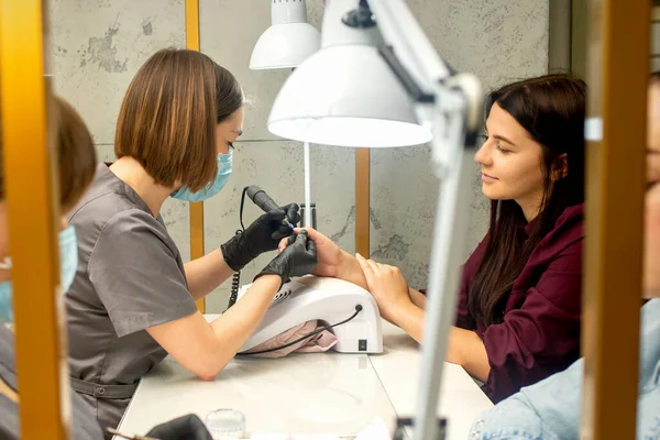Lastik eldivenli manikür ustası bir manikür salonundaki ojeyi çıkarmak için elektrikli tırnak törpüsü uyguluyor.