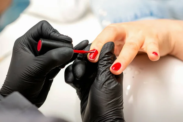 指甲清漆画 美容院一位美容师穿着橡胶黑色手套 在女性指甲上涂红色清漆的美容师的近照 — 图库照片