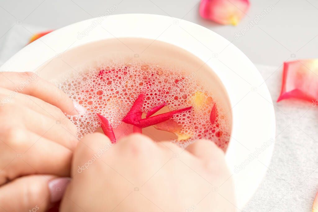Female hands in a bowl of water with pink petals of rose flowers in spa